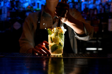 woman at bar makes crushed cocktail with slices of citrus and ice.