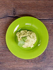 Fresh avocado pasta with parsley leaves on a green plate.