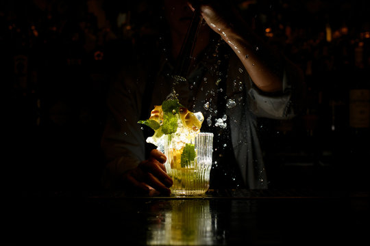 woman at dark bar energetically crushed cocktail with slices of citrus and ice.