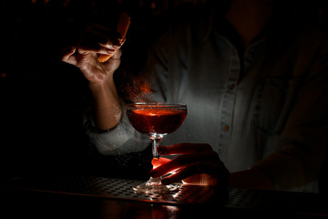 Woman barman gently sprinkles citrus juice on wineglass with cocktail at bar