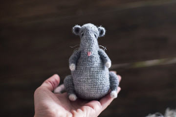Handmade knitted toy. Amigurumi gray rat toy and on the wooden background . Crochet stuffed animals.