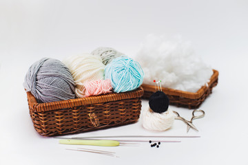 Fototapeta na wymiar Women's hobby. Crochet and knitting. Working space. Blue, gray, pink, milk yarns in basket, knitting needles, scissors, crochet hook on the white background.