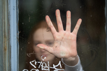 Quarantined indoor closed young girl with hand in the glass blurred in the background