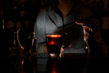 Woman barman decorates red cocktail with spikelet using tweezers