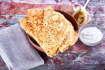 pancakes on yeast lie on a dish, next to a fork, sour cream, textile napkin