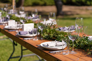 Beautifully decorated wooden table in a summer open-air cafe. Green branch and fresh flowers table decoration