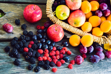 Harvest. Ripe apples, apricots, plums in a wicker basket, blackberries, raspberries, gooseberries on the wooden table in the garden on a Sunny summer day . Natural dessert. 