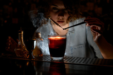 Woman barman accurate decorates red cocktail with spikelet using tweezers