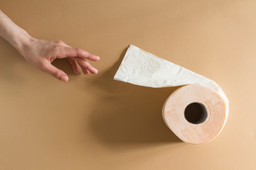 young woman reaching out for a roll of toilet paper peach beige color on beige background