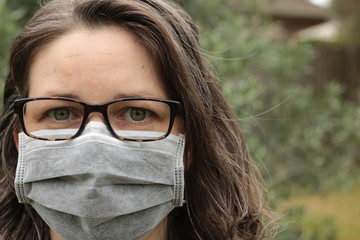 Young Australian woman wearing glasses and a paper surgical protective face mask to guard against catching or spreading infectious diseases and viruses in a public park, Victoria, Australia
