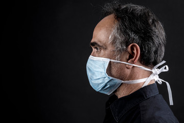 Profilo di uomo che indossa una mascherina azzurra, isolato su sfondo nero con espsessione molto seria