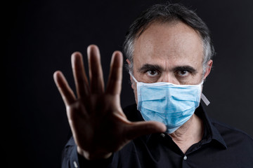 uomo in camicia nera che indossa una mascherina azzurra, isolato su sfondo nero fa cenno di stop con la mano
