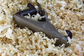 An old fashioned wood plane lies amongst the wood shavings it created.