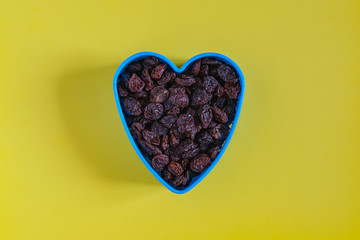 Raisins are poured in the shape of blue in the shape of a heart and located in the center on a yellow background in the style of minimalism and flat lay.