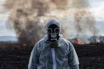 A man in a gas mask in a chemical protective suit shrouded in smoke is walking in a dangerous radioactive zone. A Stalker soldier. Post-Apocalypse. Nuclear war. Environmental disaster.