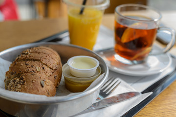 Breakfast or meal in the cafeteria. On a tray lies freshly baked bread with seeds, next to butter and sauce. Black tea with lemon and freshly squeezed orange juice with a straw in a disposable glass.