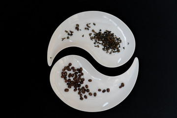 Two white plates with black coffee beans and dried leaves of green tea on black background, top view