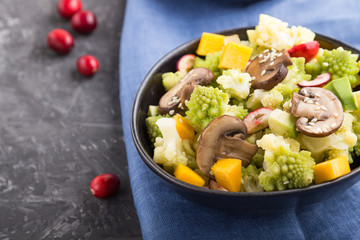 Vegetarian salad from romanesco cabbage, champignons, cranberry, avocado and pumpkin on a black concrete background. side view, selective focus.