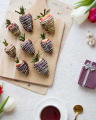 Chocolate-covered strawberries, coffee and flowers on the table. Light photo, top view.
