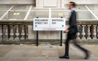 London civil servant. A suited office worker passing a street sign for Parliament Street and Whitehall in the civil service district of Westminster. - 333422407