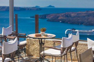 Cafe on the terrace overlooking the sea. Santorini island, Greece. Luxury summer travel background, chairs and table over sea view. Amazing vacation, tourism landscape