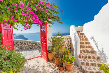Fantastic summer vacation landscape. Santorini white architecture with red gate and pink flowers. Tranquil travel background, luxury tourism scenery, stone stairs under blue sky.