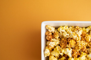 caramel popcorn in a square bowl with an orange background.