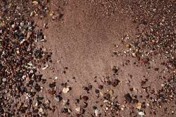 Close-up picture of sandy beach sand with small colorful stones rocks and foamy waves of sea water. Natural texture tropical background.