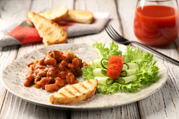 Beans in tomato sauce with garlic and cilantro, served on a white plate with lettuce, thinly sliced ​​cucumbers, tomatoes, fried toast from wheat bread and a glass of tomato juice. Real food.