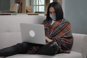 Pan left view of young african american woman wearing medical mask and warm plaid using laptop during remotely work at home due to coronavirus pandemic. Stay home remotely office coronavirus social di