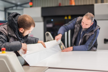 Two technicians glue poster to foam. Semi automatic gluing machine
