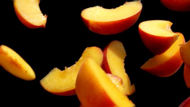 Slices of peaches are flying diagonally on the black background in slow motion