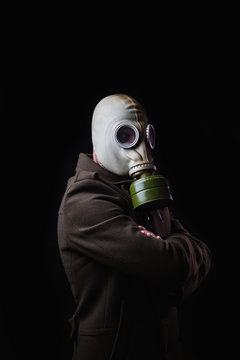 Hombre joven con m&aacute;scara de gas y un abrigo largo sobre un fondo oscuro