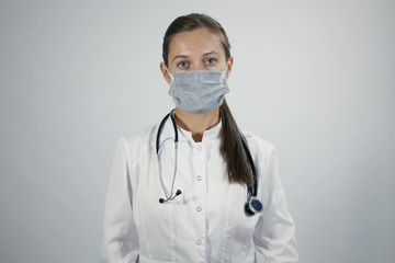 Portrait of young adult female doctor wearing protective medical mask puts on the neck stethoscope and looking straight to the camera. Isolated background