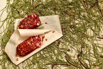 Dried sausage made of beaver meat cut with slices on parchment with pine buds on the left flooring...