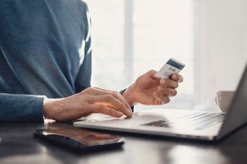 Man using laptop computer and holding credit card, young businessman or entrepreneur working at home, online shopping, e-commerce, internet banking, finance and freelance concept