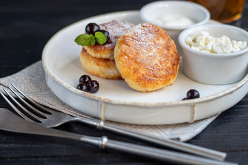 Homemade pancakes with cottage cheese on a dark lantern with black currants and cranberries. Breakfast for the whole family. Healthy vegan food concept.