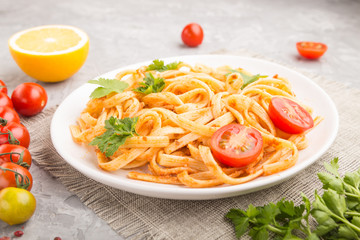 Semolina pasta with tomato pesto sauce, orange and herbs on a gray concrete background. Side view, selective focus.
