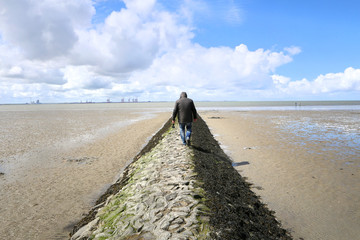 Ein gutaussehender Mann spaziert allein am Deich an der Nordsee und genie&szlig;t die frische Meeresluft sowie die Ruhe an der wundersch&ouml;nen deutschen K&uuml;ste