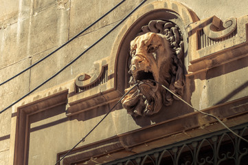 A lion's head sculpted in stone on a facade with wires hanging from its mouth