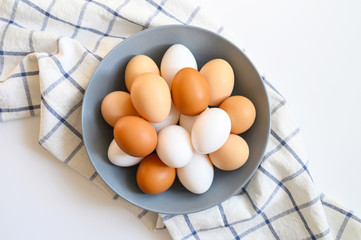 chicken eggs white and brown color in a gray plate on a checked kitchen towel on a white table....