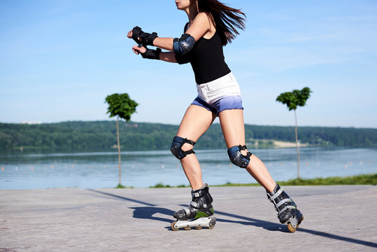Young woman, roller-blading on rollerdrome. Tan legs, wearing roller-skates and protective equipment, showing the process of riding on metal platform.