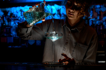 Woman at bar pours cocktail into glass