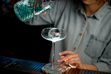 Close-up woman at bar accurate pours cocktail into glass with ice.