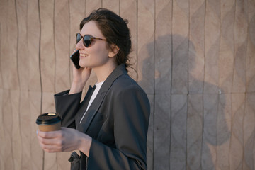 Business woman discusses work issues by phone in the park. young woman drinks soy coffee in the park and speaks on the phone