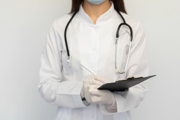Clouse-up female doctor in a protective medical mask and gloves, writes the diagnosis to the clients card