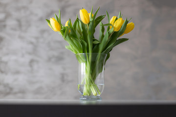 Bukiet żółtych tulipanów w wazonie na stole.