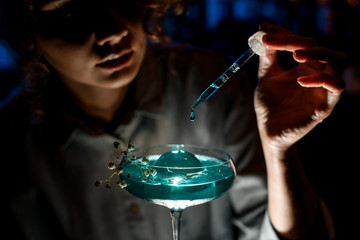 Close-up woman at dark bar adds cocktail ingredient using pipette