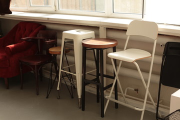 various different chairs stools stand along the wall by the window