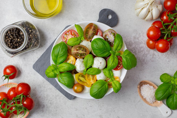 Italian, traditional caprese salad with cherry tomatoes, mozzarella and basil. Salad ingredients, olive oil, spices, salt. Organic and natural food concept. Light background. Top view. Flat lay.
